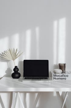 A clean and modern workspace featuring a laptop, vase, and decorative elements on a table.