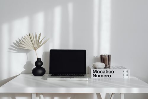 Free A simple and elegant workspace setup with a laptop, vase, and decor on a white table. Stock Photo