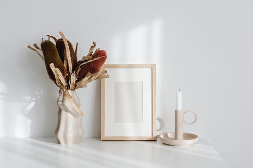 Free Elegant minimalist decor featuring a candle, frame, and vase on a white tabletop, bathed in natural light. Stock Photo