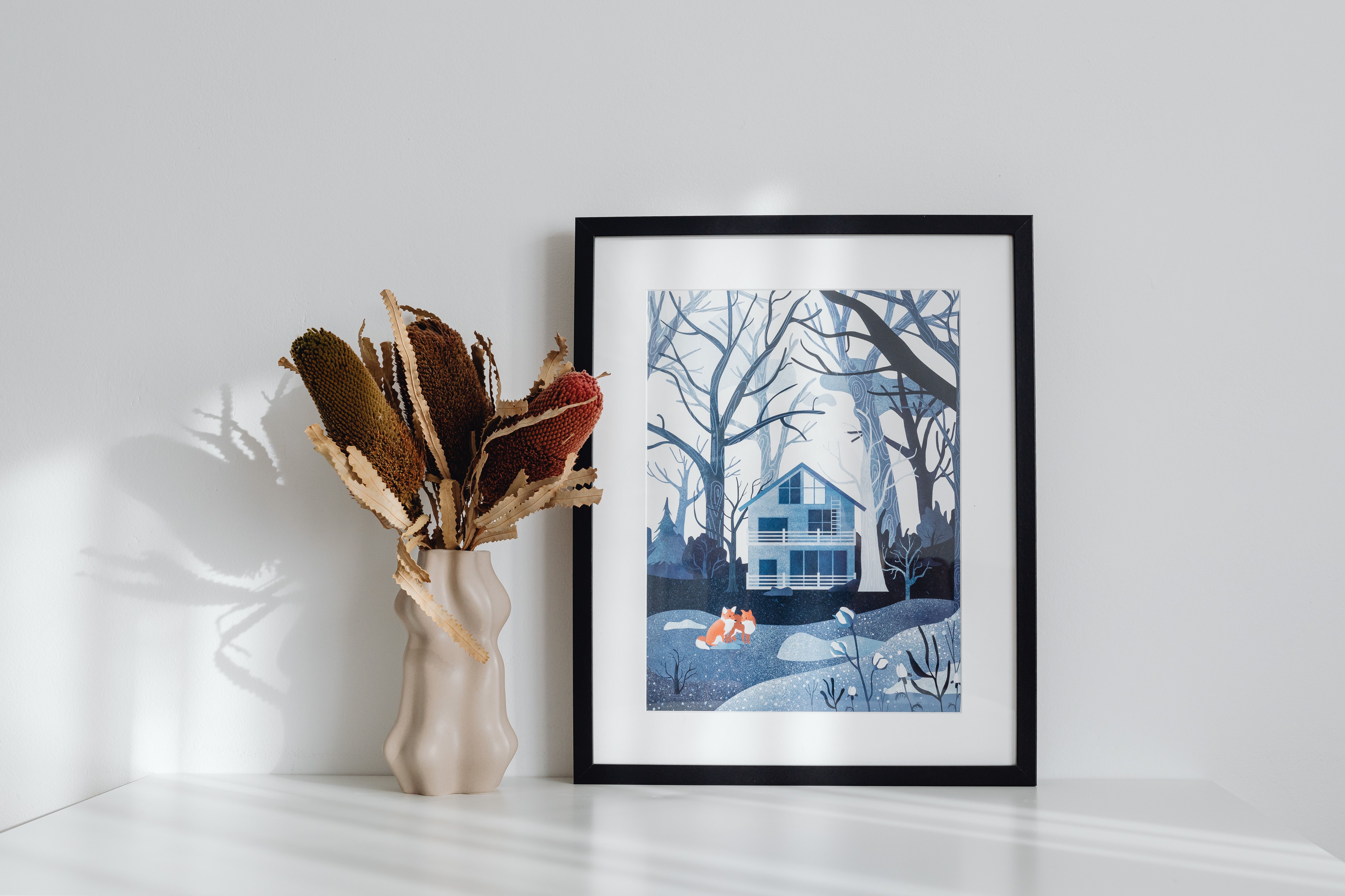 Elegant minimalist interior featuring framed art and decorative vase on a white surface.