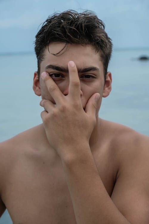 Thoughtful topless guy covering mouth with hand near sea