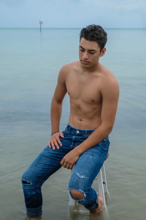 Free Pensive young shirtless male in jeans sitting on stool in rippling ocean in daytime under gray sky Stock Photo