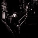 在一张黑白照片中，一位戴着贝雷帽的老妇人坐在光线昏暗的城市环境中