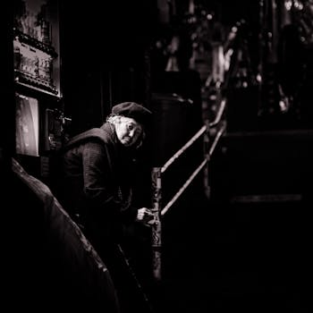 在一张黑白照片中，一位戴着贝雷帽的老妇人坐在光线昏暗的城市环境中