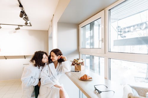 A romantic couple in bathrobes enjoys a cozy morning by the window with coffee and pastries.