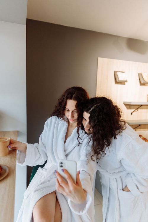 Free A couple in white bathrobes taking a selfie while enjoying morning coffee indoors. Stock Photo