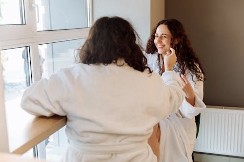 Two women laughing and enjoying a relaxed morning in bathrobes by the window.