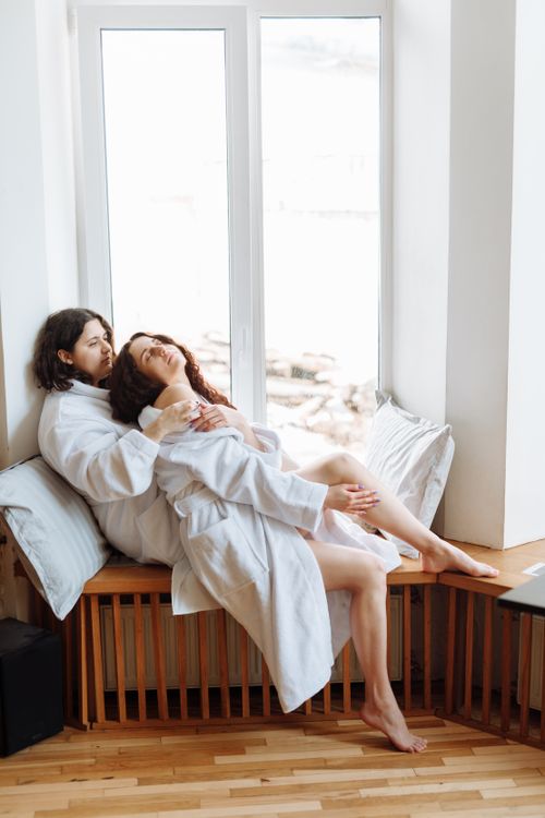 Free Two women in robes share a loving moment by a window in a bright room. Stock Photo