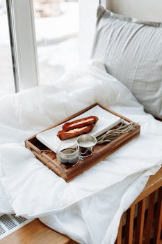 A wooden tray with pastries and coffee on a cozy bed by a window, perfect for a relaxing morning.