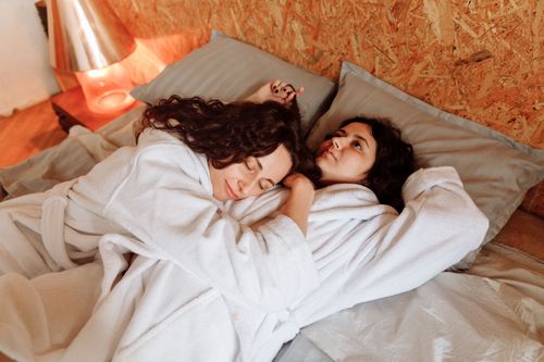 Free A loving LGBTQ+ couple in bathrobes embracing on a bed, evoking warmth and intimacy. Stock Photo