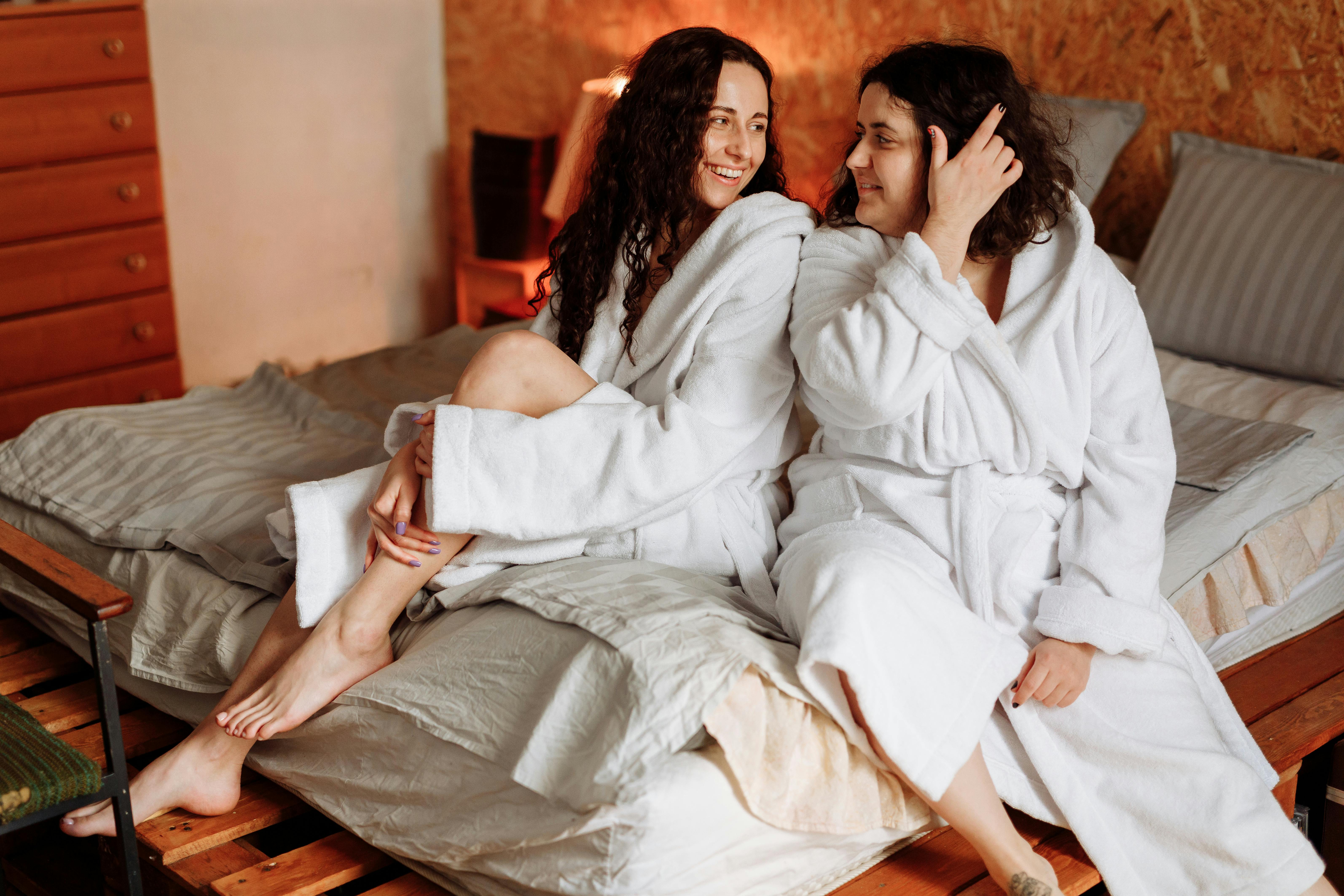 2 Women in White Robe Sitting on Bed · Free Stock Photo