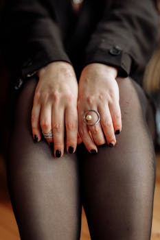 Elegant hands with rings and manicured nails resting on black stockings in a close-up shot.