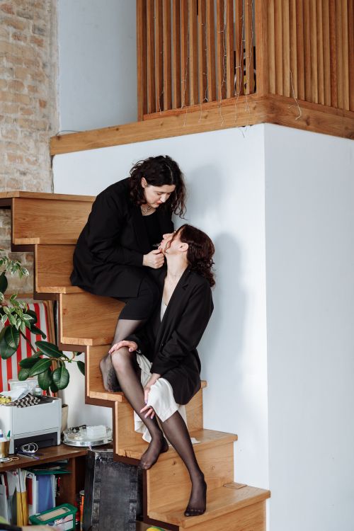 Free Two women share a loving moment on a wooden staircase indoors. Stock Photo