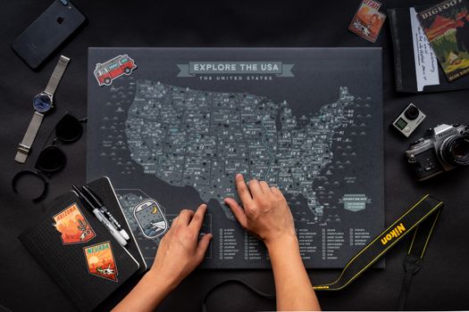 Hands interacting with a USA map alongside travel essentials including a notebook and camera.