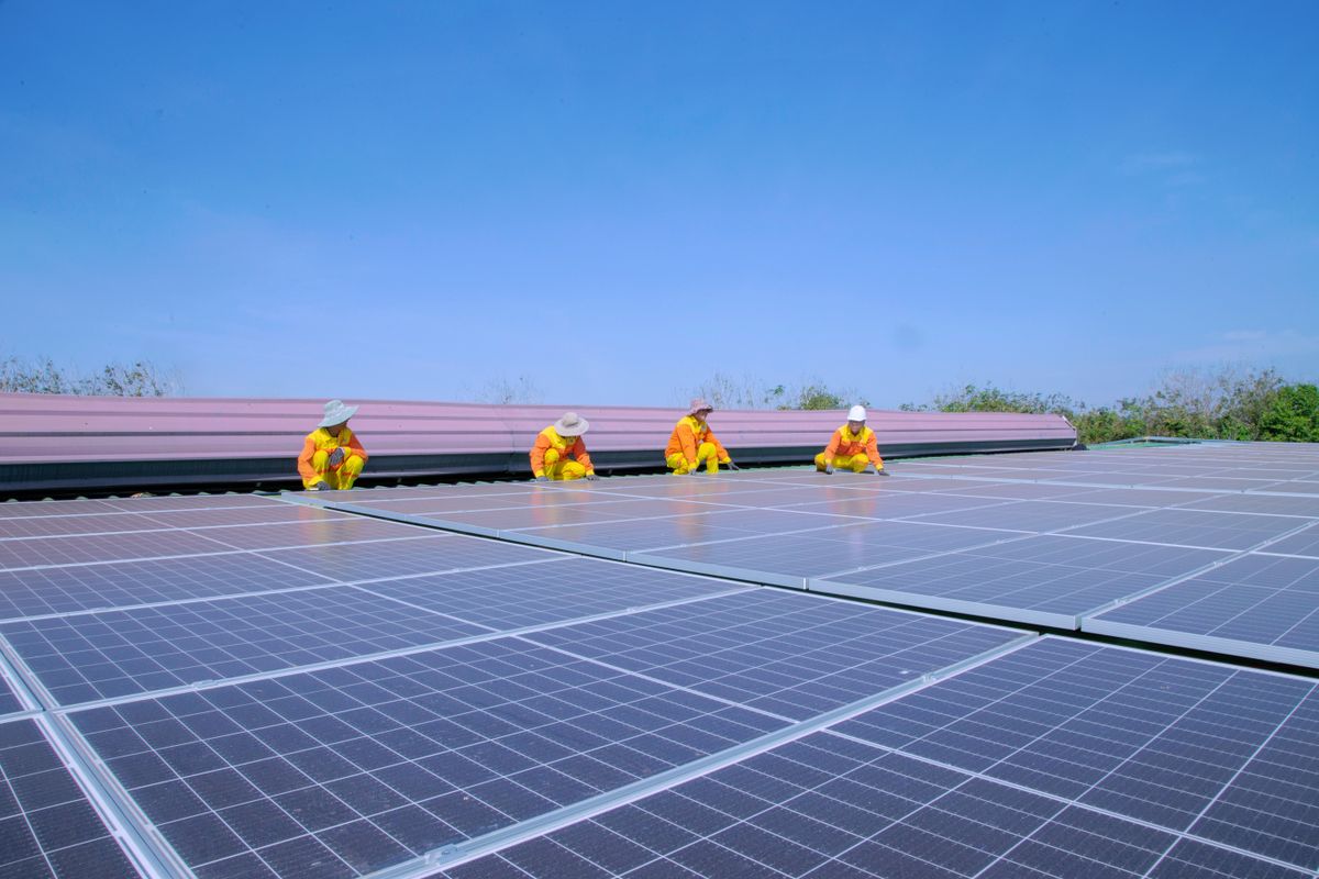 Technicians in Southeast Asia installing photovoltaic solar panels under a clear sky, the charging principle behind solar light towers