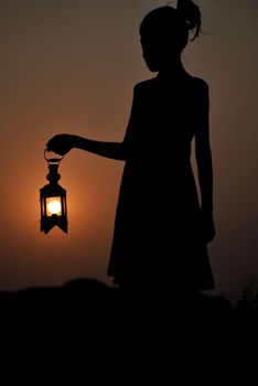 Captivating silhouette of a girl holding a lantern against a dramatic sunset sky, evoking mystery and tranquility.