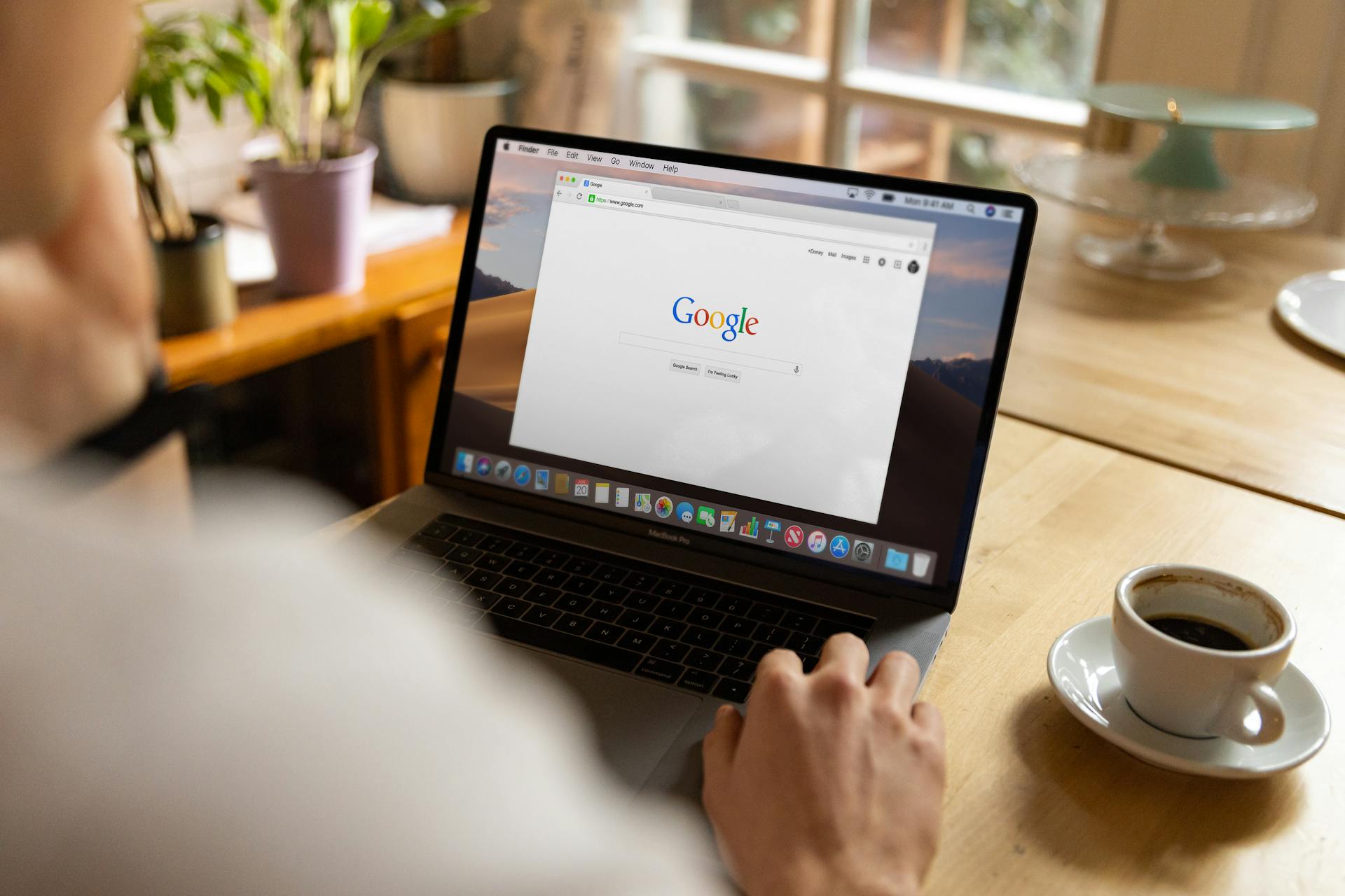 An adult using a laptop indoors, browsing Google at a wooden table with coffee.