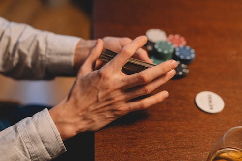 Free A Person Holding a Playing Cards Near the Wooden Table Stock Photo