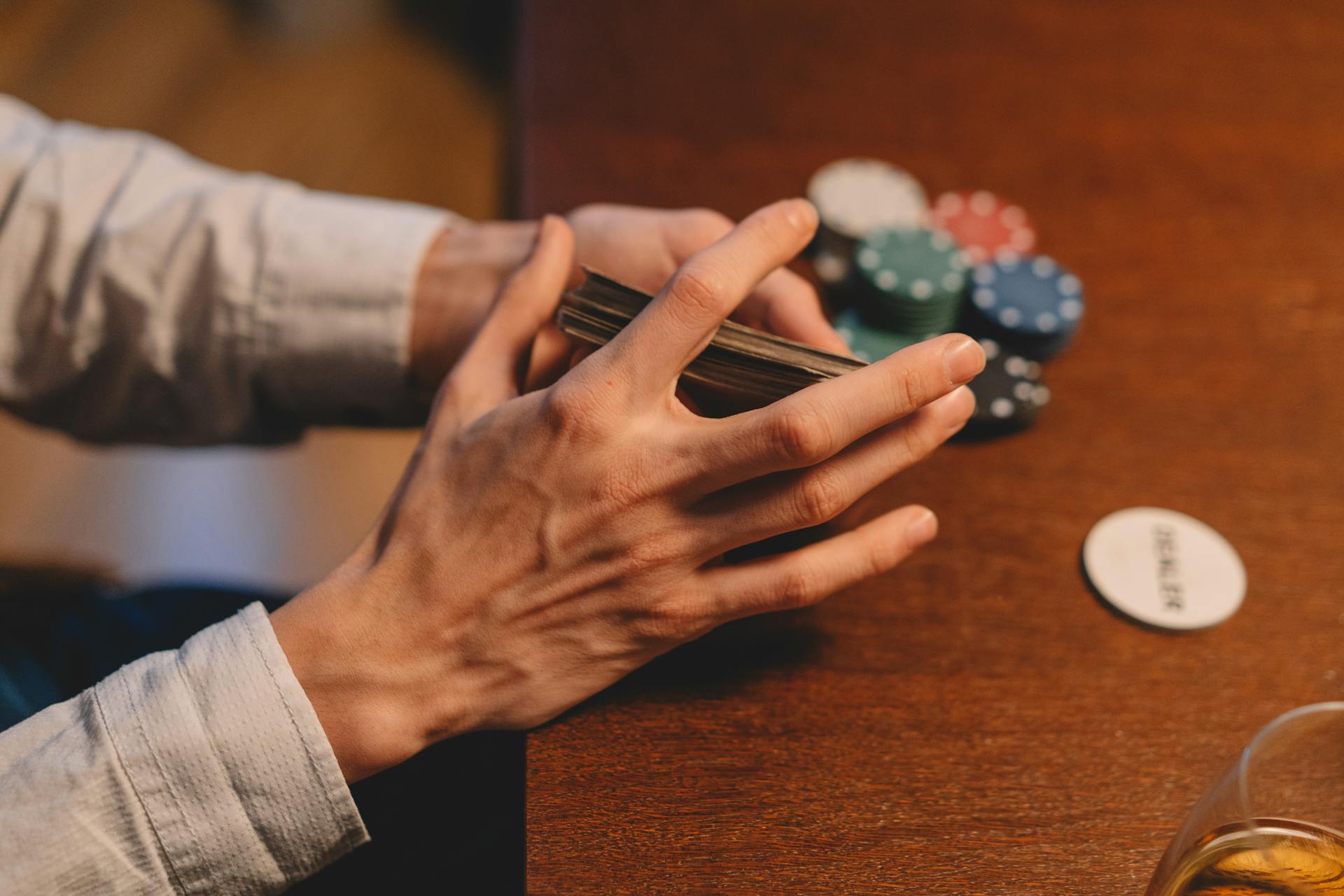 Hands holding cards and poker chips on a wooden table, capturing the gaming atmosphere.