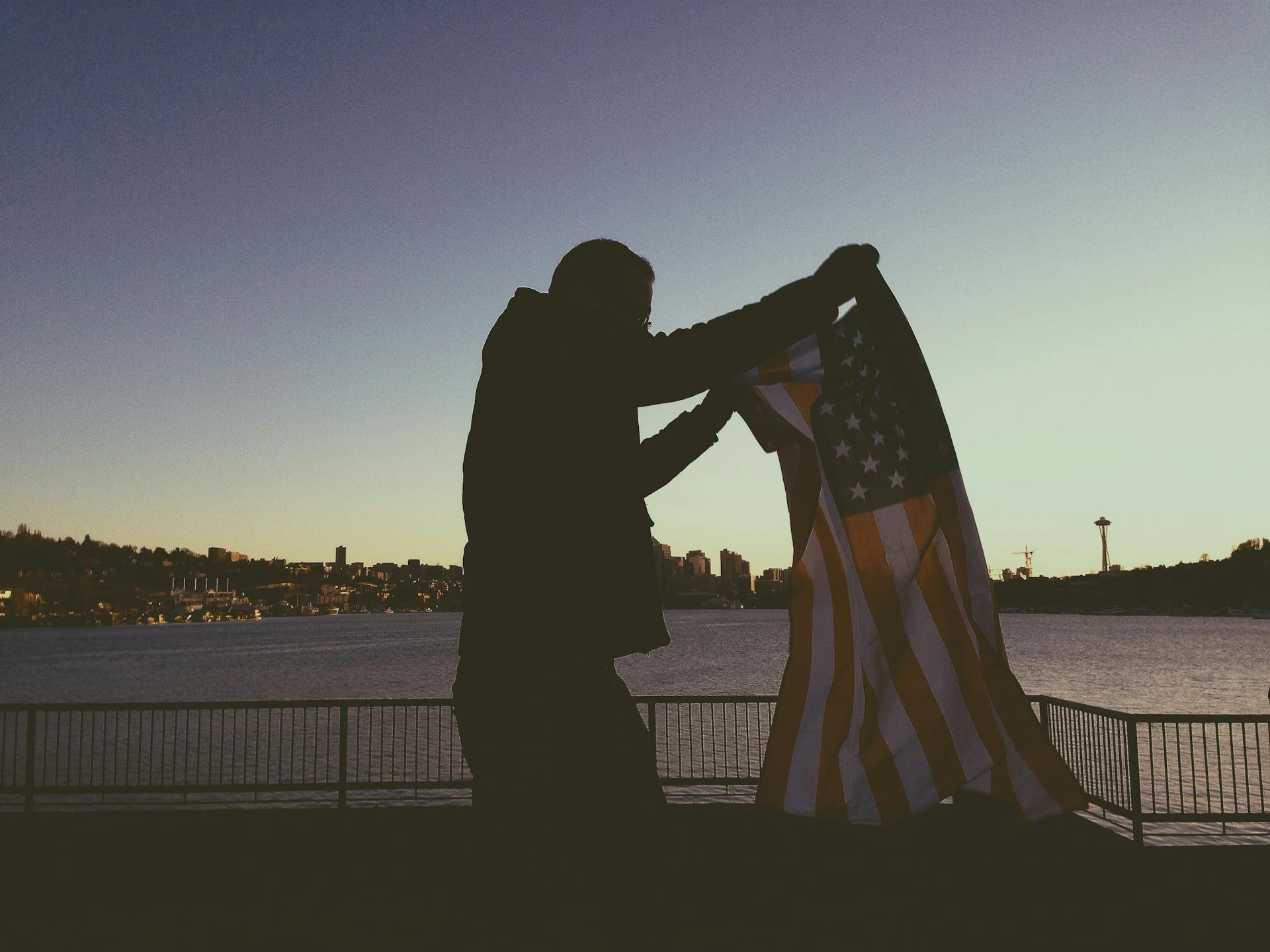 Person holding an American flag with Seattle skyline in the background at sunset.