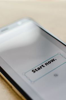 A close-up photo of a smartphone displaying 'Start Now', emphasizing digital interaction.