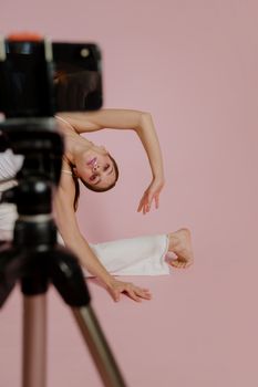 A stylish model striking a flexible pose during a studio photoshoot against a pink background.