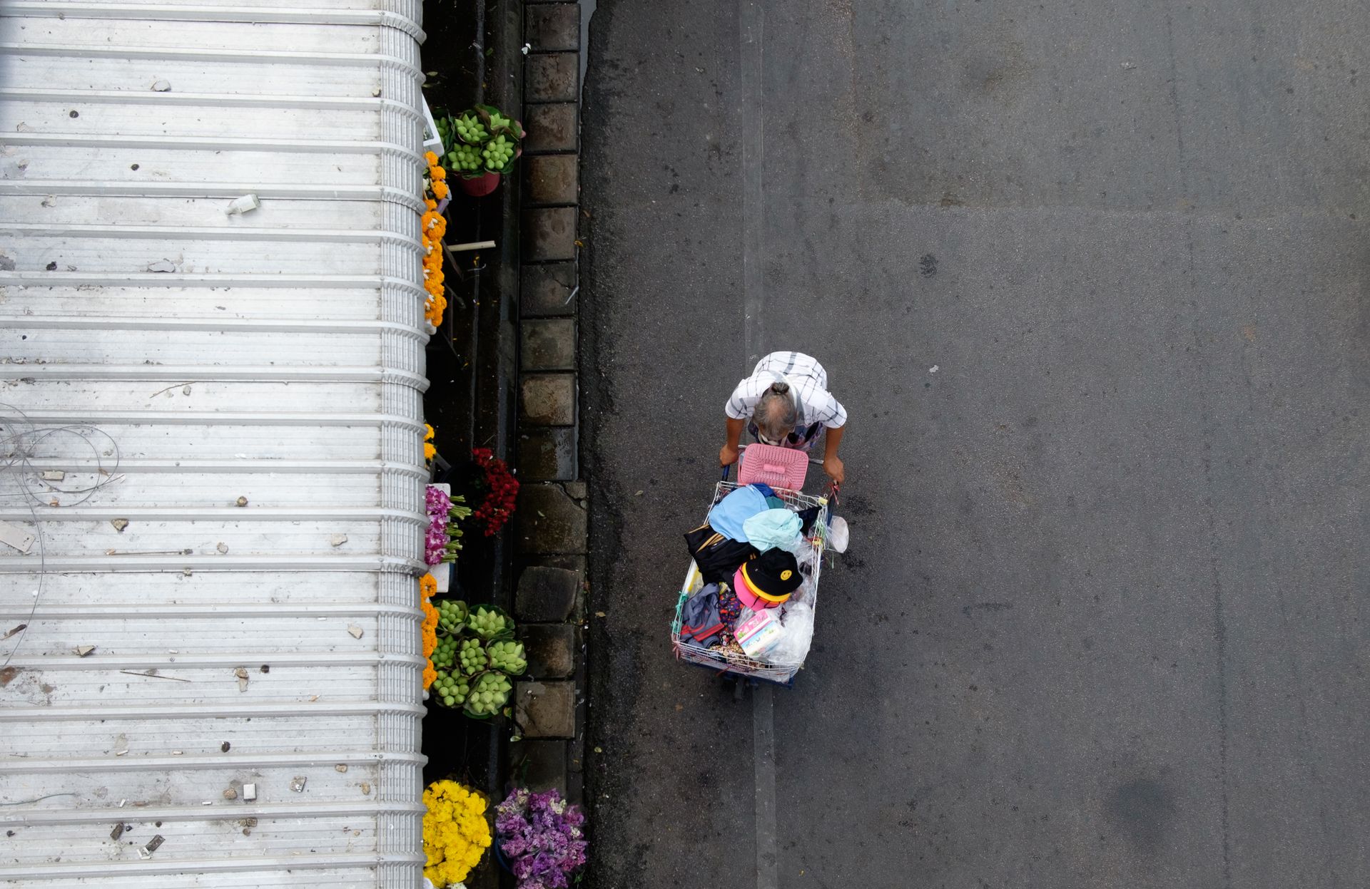 Overhead view of an elderly man pushing a cart in a Chiang Mai street beside a flower shop.