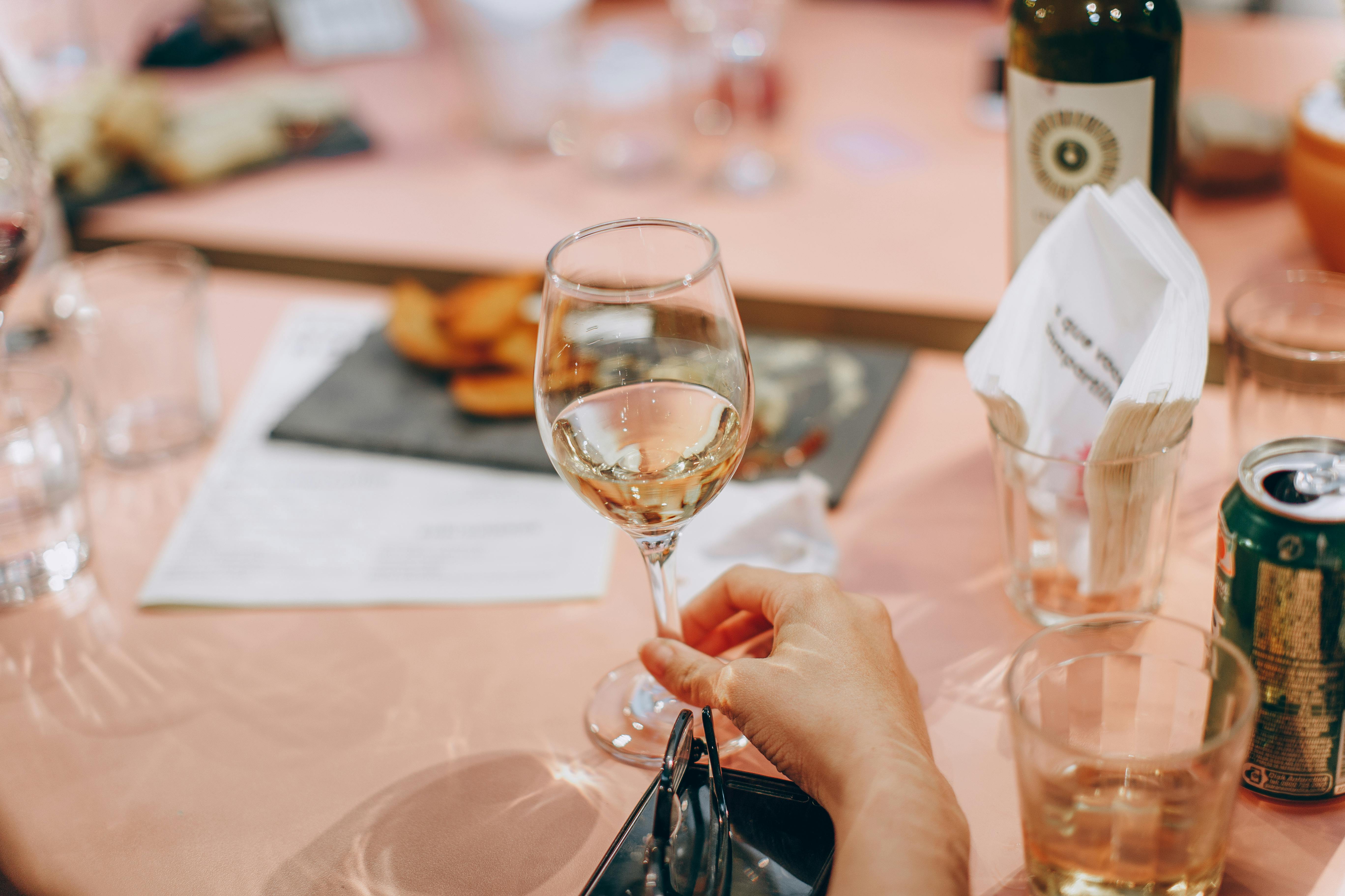 person holding wine glass near clear shot glasses