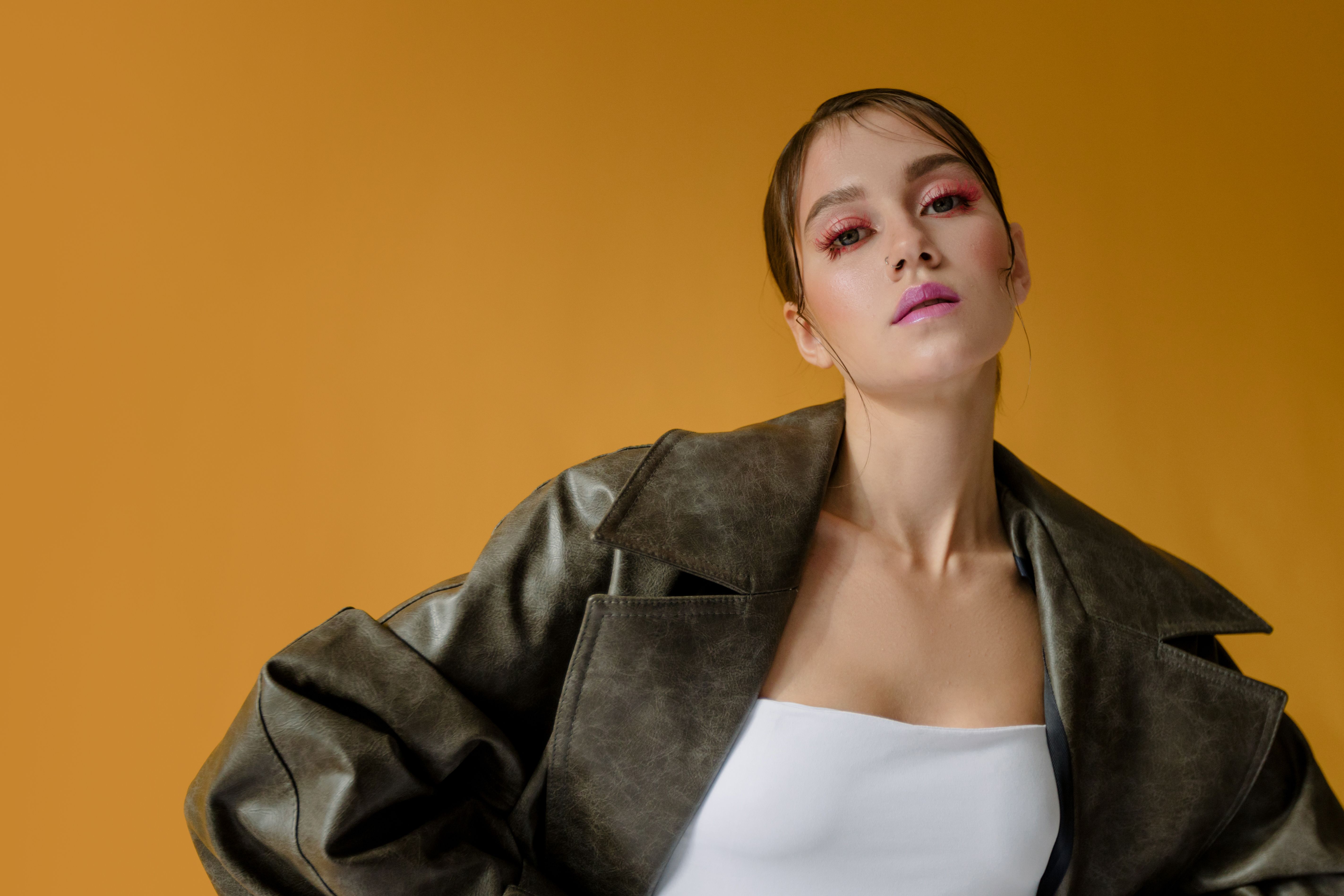 Fashionable woman posing against a yellow background, showcasing trendy style and makeup.