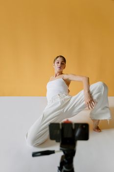 Fashionable woman poses in a studio, capturing creative content using a smartphone.