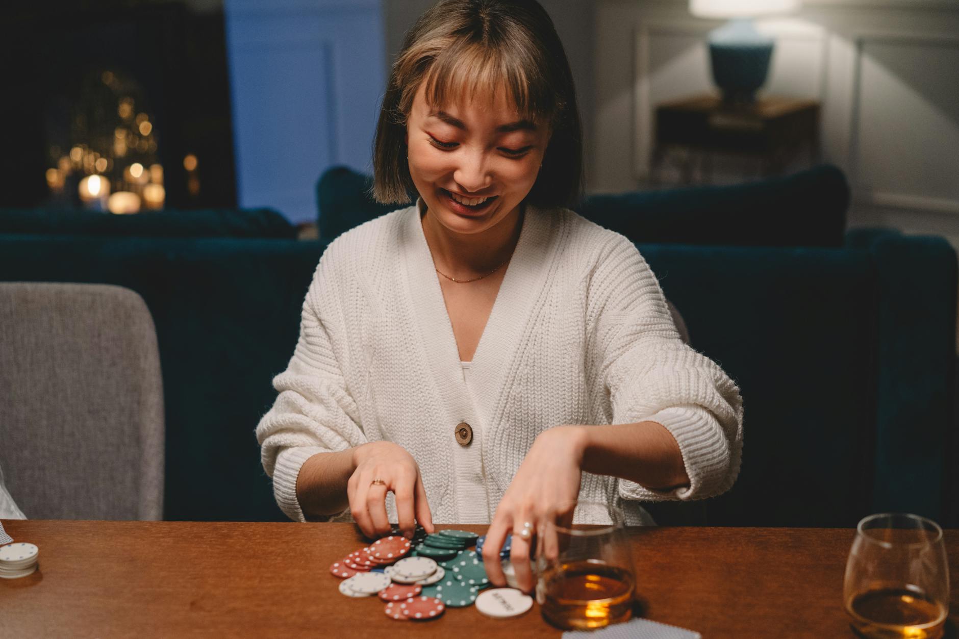 Asian woman in a cozy setting enjoying poker with whiskey.