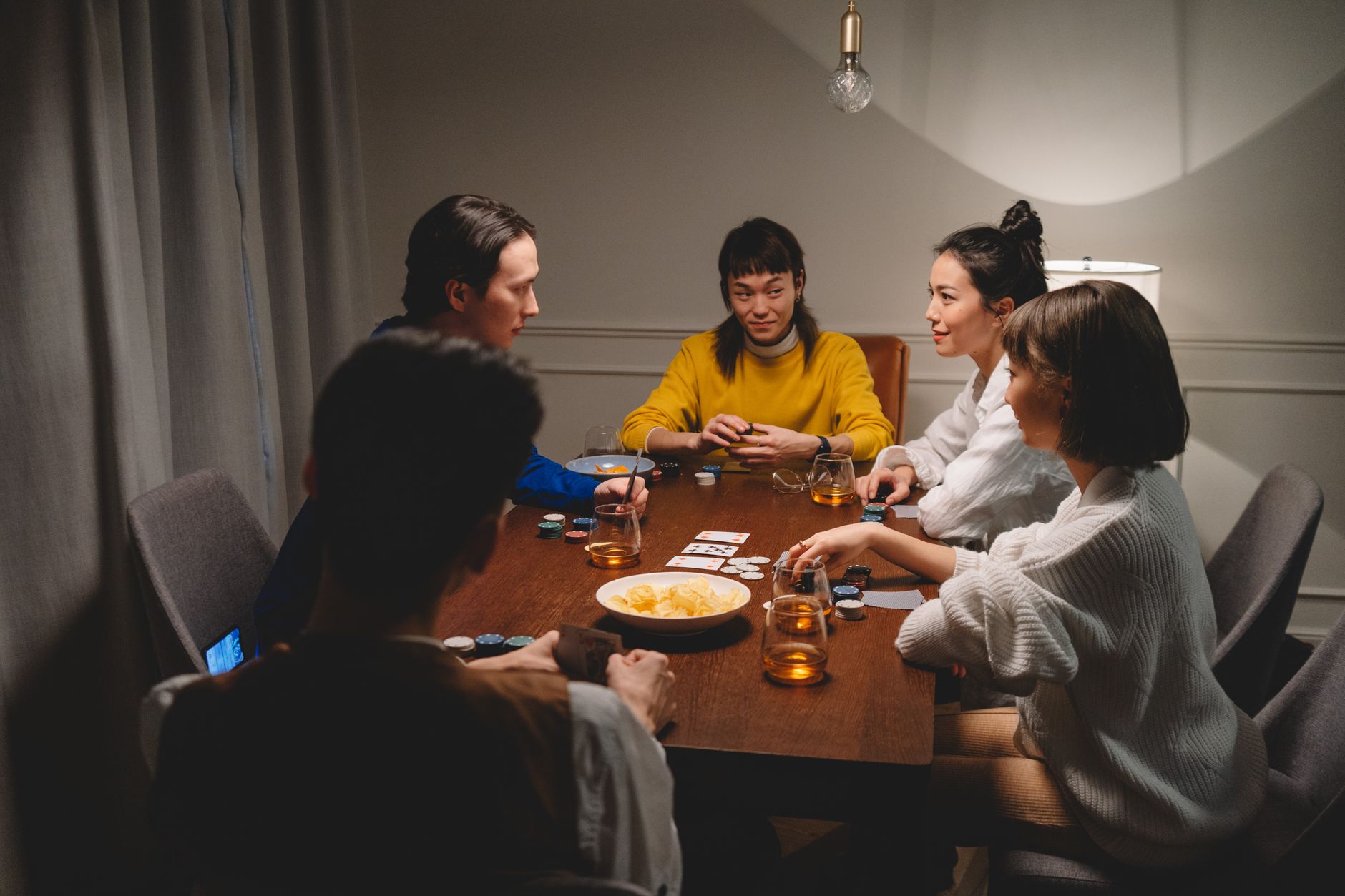 A group of friends playing poker indoors, enjoying drinks and snacks.