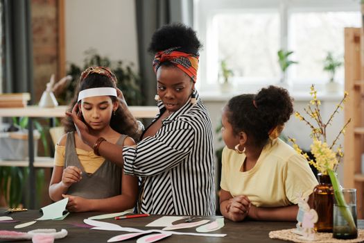 A woman and two girls engage in a fun crafting session with Easter decorations on a table.