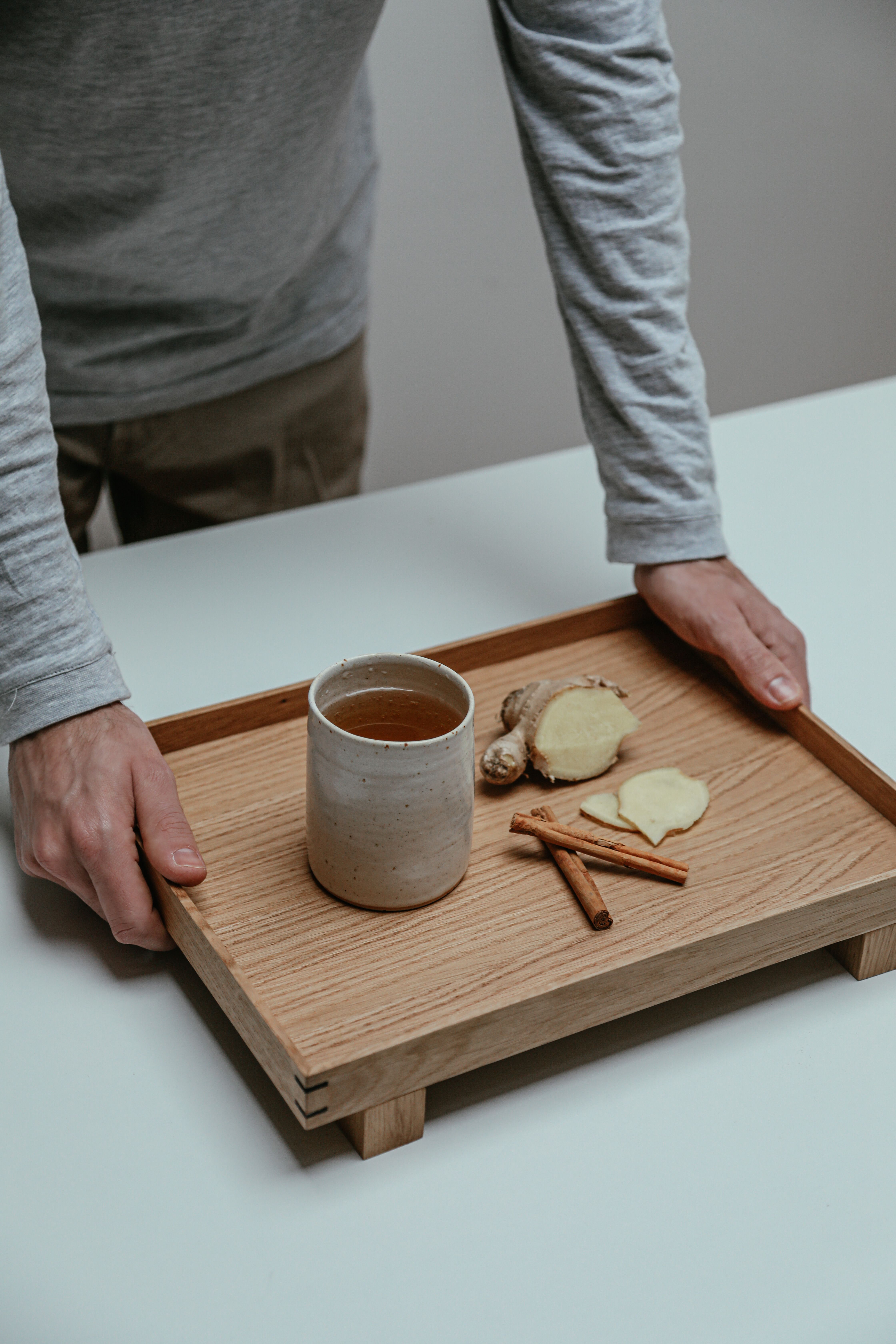 A person serves herbal tea with ginger and cinnamon on a wooden tray indoors.