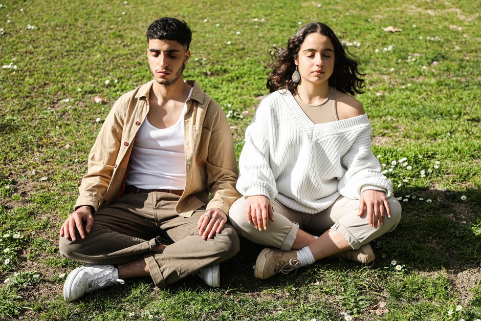 Man and woman meditating outdoors with closed eyes on a sunny day, enhancing mindfulness and relaxation.