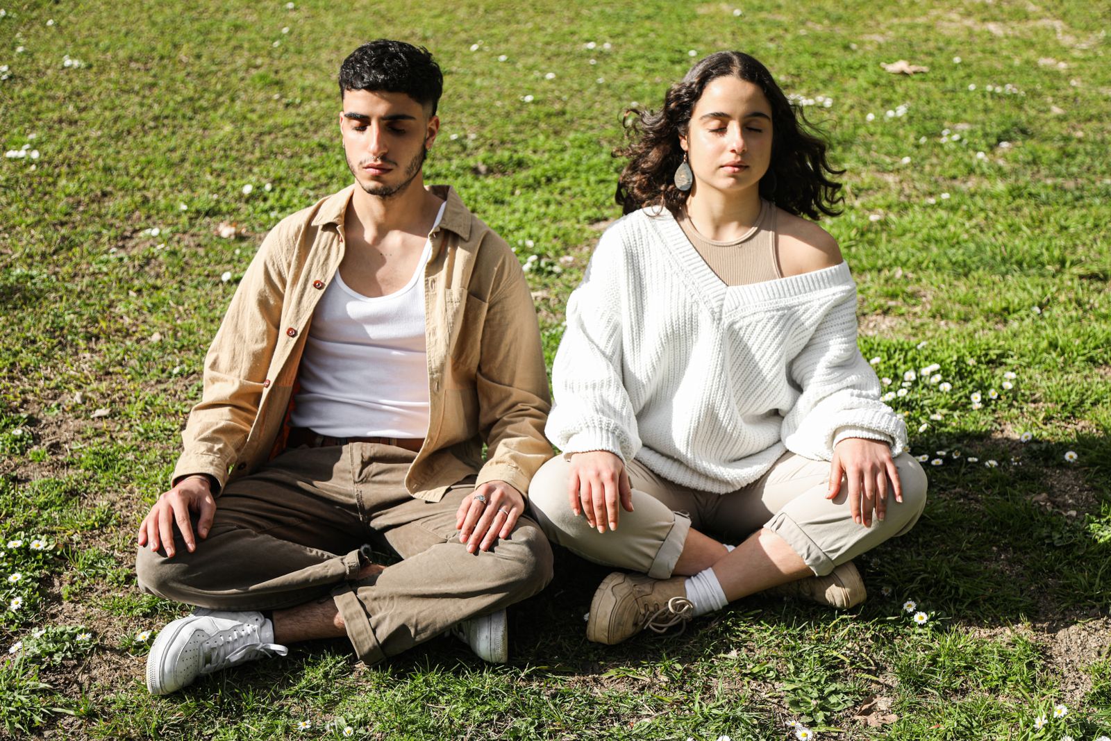 Man and woman practicing a seated meditation technique outdoors on a sunny day