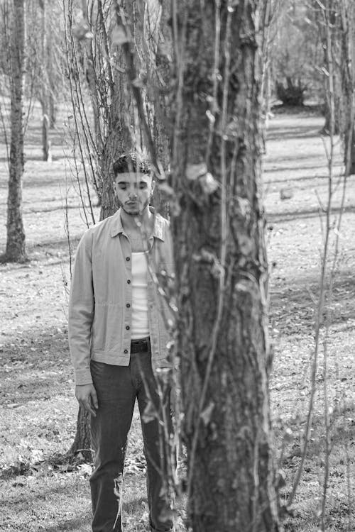 Grayscale Photo of Man Standing Beside a Tree 