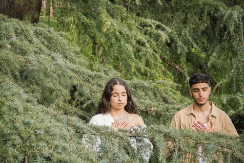 Free A couple meditates peacefully amidst lush green foliage, capturing a serene outdoor moment. Stock Photo