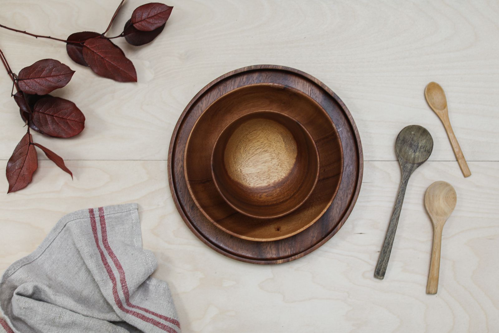Flat lay of wooden bowls, spoons, and leaves on a light surface, creating a rustic aesthetic.