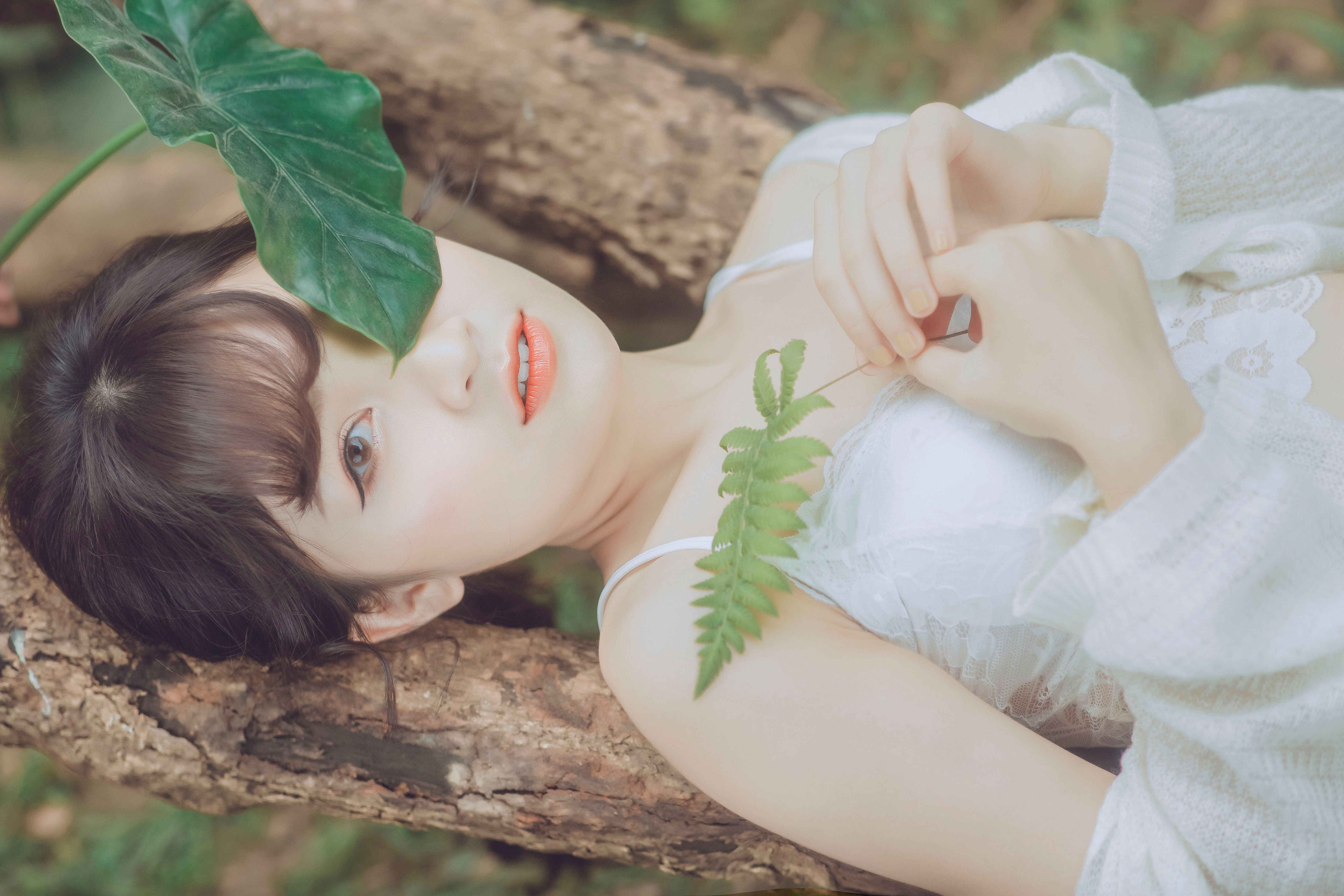 A serene portrait of a young woman lying on tree bark, surrounded by lush green leaves.