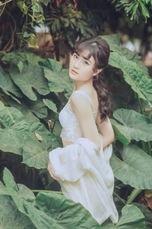 Free A young woman in stylish attire poses gracefully amidst large green leaves, exuding beauty and elegance. Stock Photo