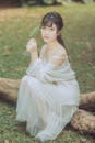 A Woman in White Spaghetti Strap Dress Sitting on Brown Wood Log