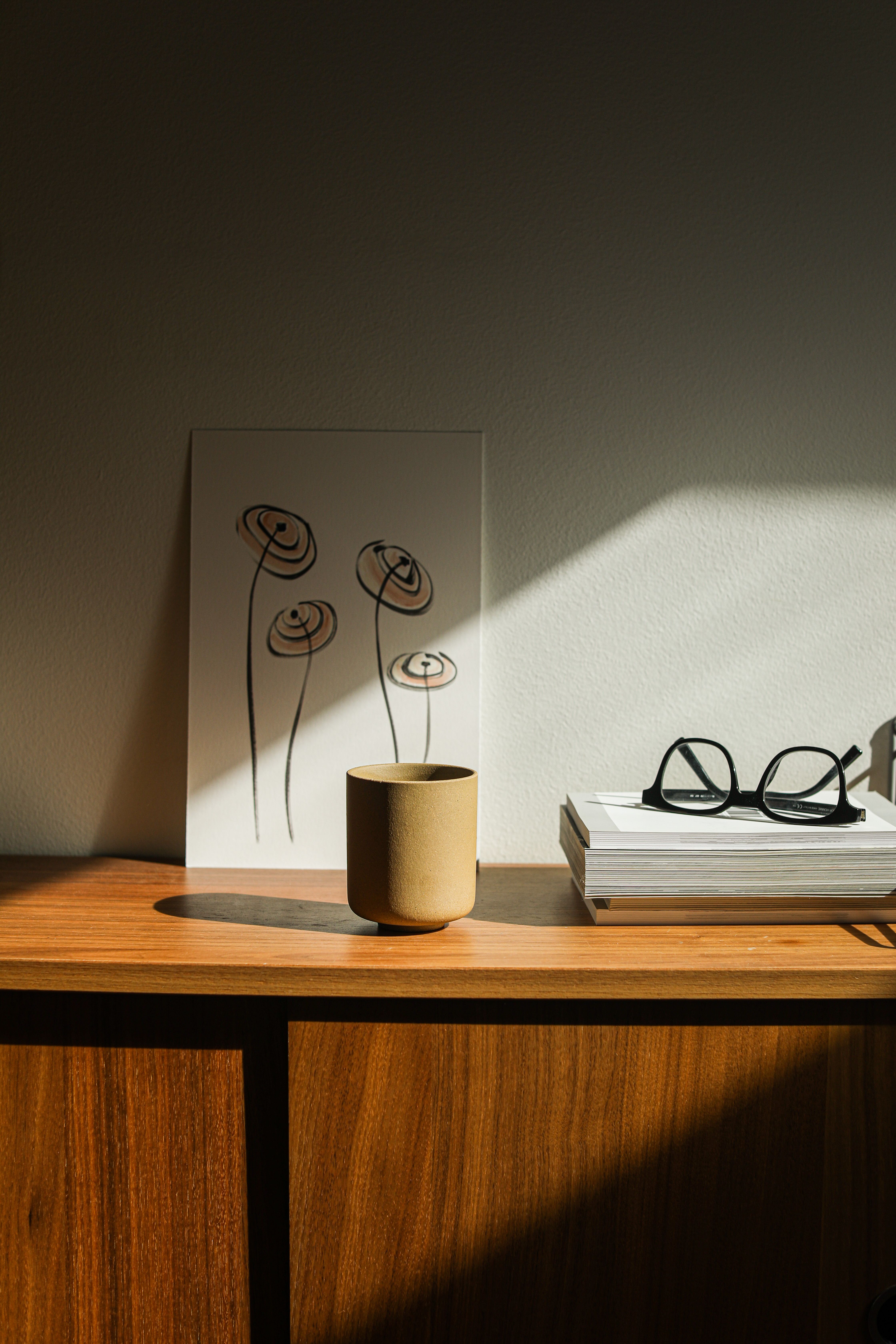 A minimalist setup featuring books, a cup, and glasses on a wooden table with light and shadow play.