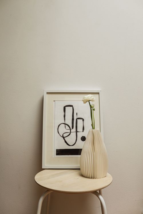 Free A minimalist arrangement featuring abstract art and a vase on a wooden stool. Stock Photo