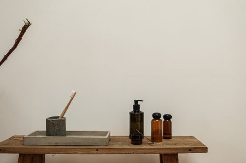 Free A rustic bathroom bench with toothbrush, soap dispenser, and bottles in a minimalist setting. Stock Photo