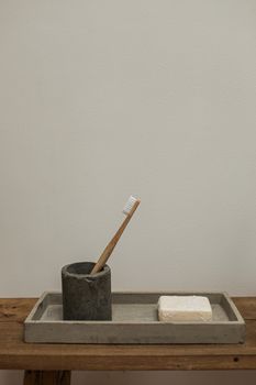 A concrete tray with a wooden toothbrush and soap in a minimalist bathroom setting.