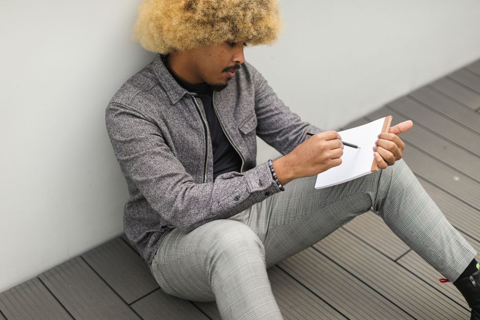 African American man deeply focused, writing thoughts in a notebook, sitting outdoors. African American man deeply focused, writing thoughts in a notebook, sitting outdoors.