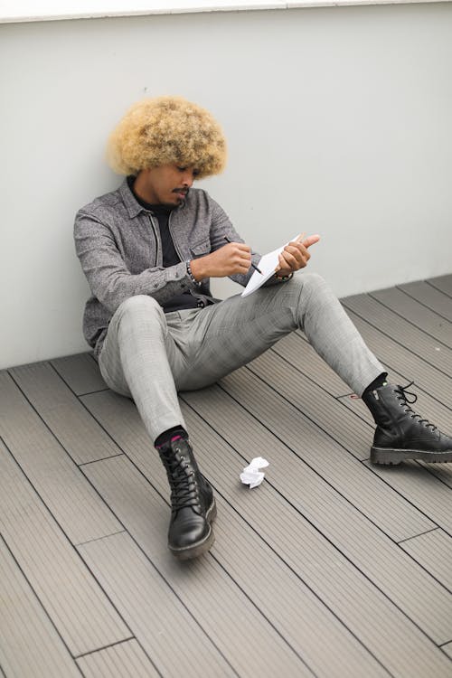 Man Sitting on the Floor while Writing on a Notebook 