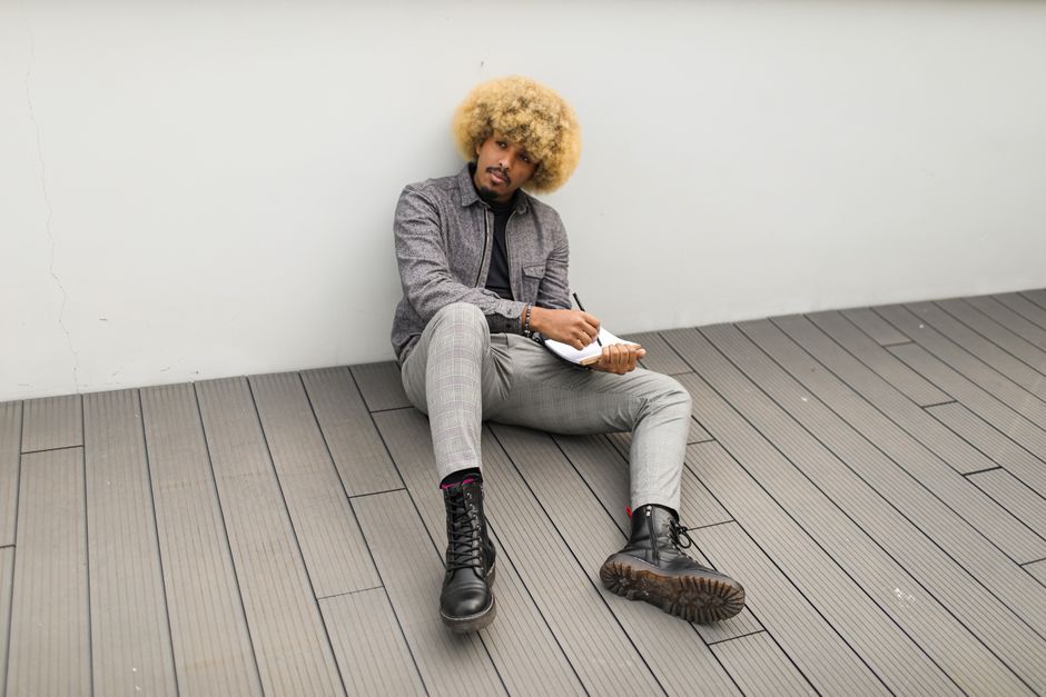 Stylish young man with afro hair and notebook sitting on wooden floor outdoors. Stylish young man with afro hair and notebook sitting on wooden floor outdoors.