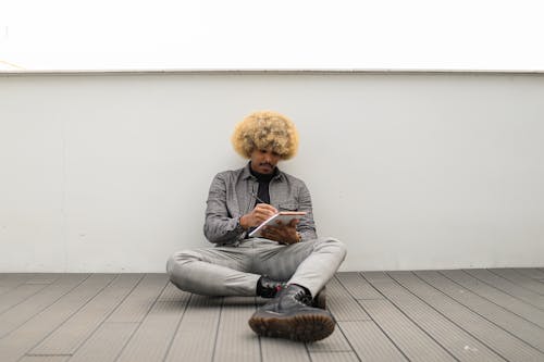 Man Sitting Alone on the Floor While Writing on a Notebook 